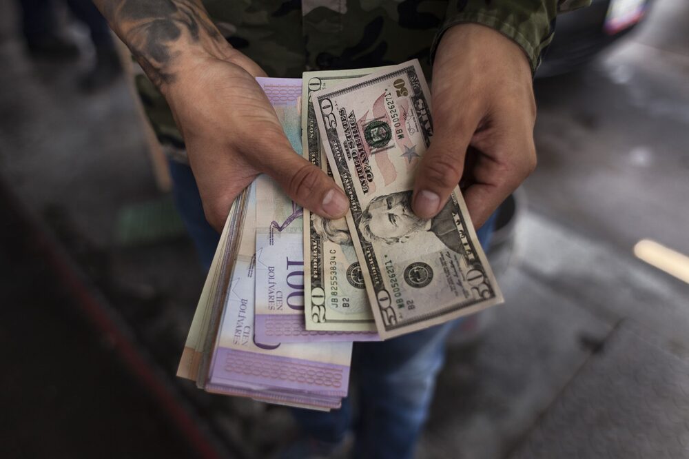 Un hombre sostiene billetes de dólares estadounidenses y un fajo de bolívares venezolanos en Caracas, Venezuela. Un hombre sostiene billetes de dólares estadounidenses y un fajo de bolívares venezolanos en Caracas, Venezuela.